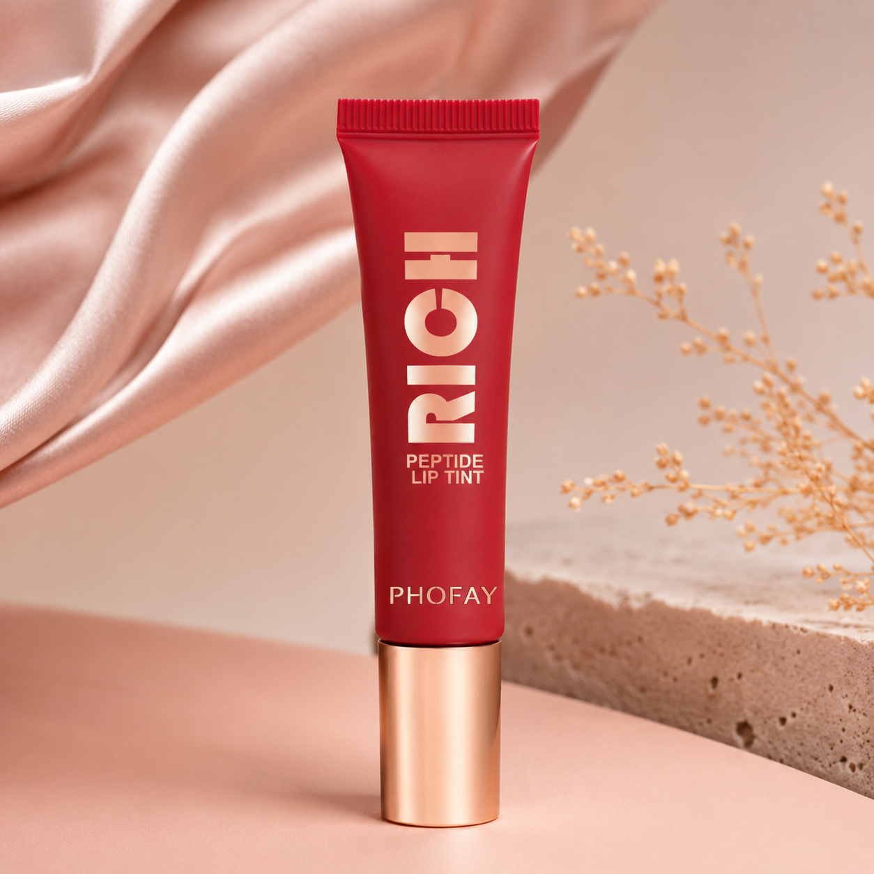Red lip tint tube with gold cap on a soft pink background
